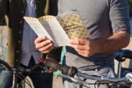 A man is holding a city map of Munich in his hands. A bike is besides him.