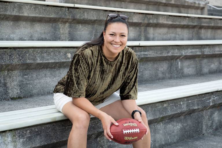 Nadine Nurasyid, the Munich ambassador for football, sits in the stands at the Dante Stadium holding a football in her hands.